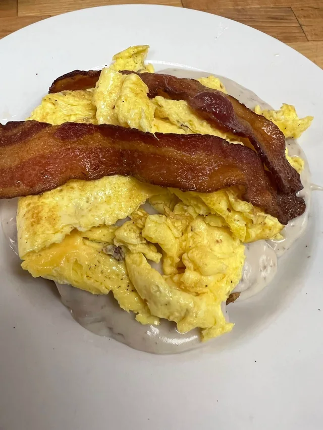 Hash bowl topped with scrambled eggs, bacon and sausage gravy.