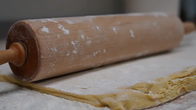 A wooden rolling pin rests on a sheet of dough dusted with flour.