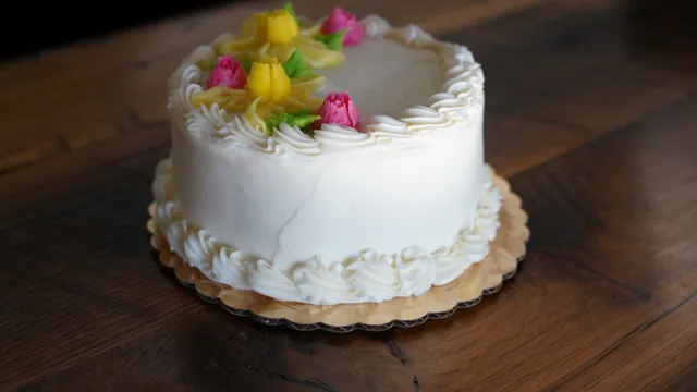 A white round cake decorated with yellow and pink icing flowers and green leaves.