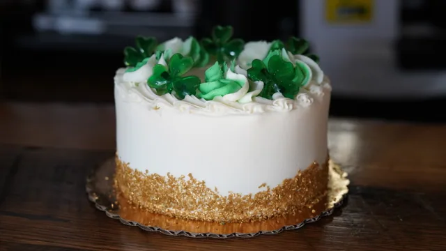 A white cake with green icing decorations and a golden crumb border.