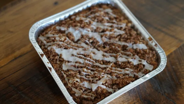 A foil tray of crumb-topped baked pastry finished with white icing drizzle.