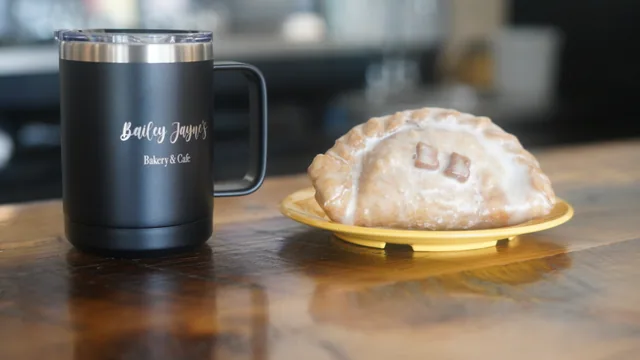 A glazed folded pastry on a yellow plate beside a Bailey Jayne’s insulated mug.