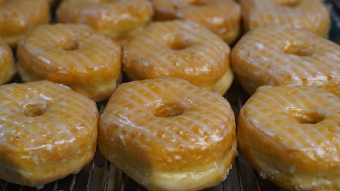 Rows of golden ring donuts coated in a thin shiny glaze.