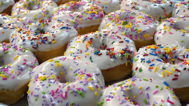 Rows of white-iced ring donuts topped with multicolored sprinkles.