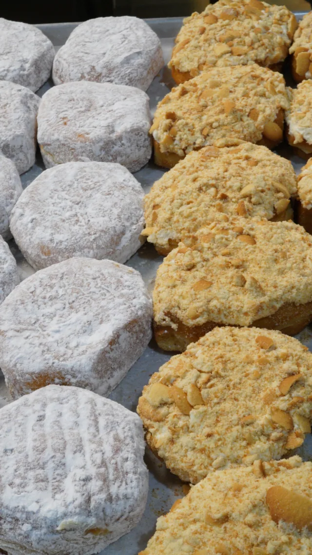 A portrait view of powdered and crumb-topped donuts arranged in the bakery case.