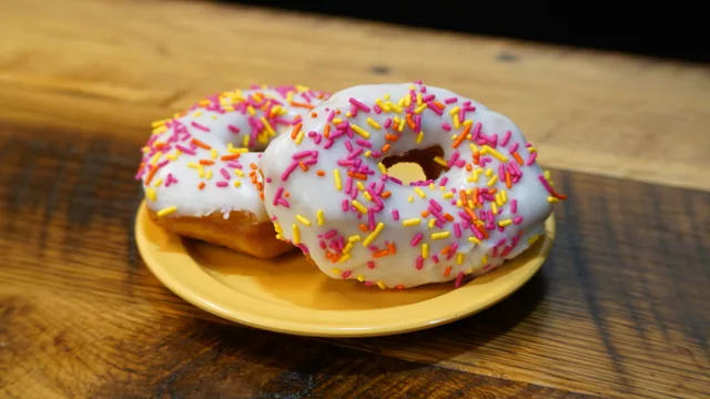 Two white-iced ring donuts covered in colorful sprinkles on a yellow plate.