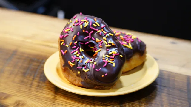 Two chocolate-iced ring donuts with colorful sprinkles on a yellow plate.