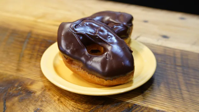 Two golden ring donuts covered in glossy chocolate icing on a yellow plate.