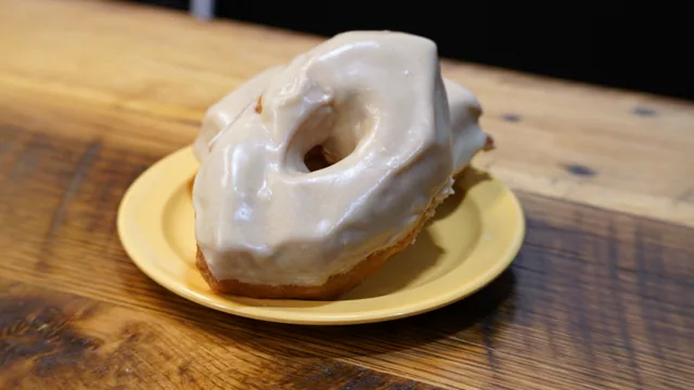 Two ring donuts covered with pale icing on a yellow plate.