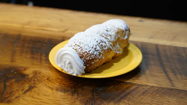 A powdered rolled pastry with a white cream swirl at its open end.