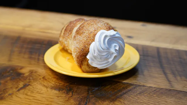 A sugar-coated rolled pastry with a large white cream swirl at its open end.