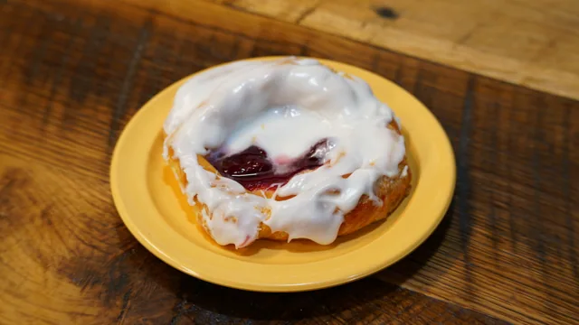 A round pastry with visible red fruit filling and white icing on a yellow plate.
