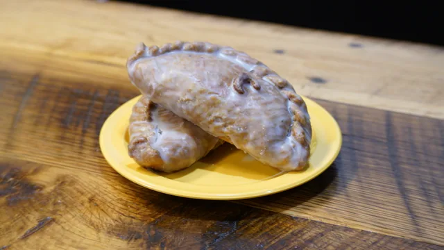 Two crimped folded pastries finished with glaze on a yellow plate.