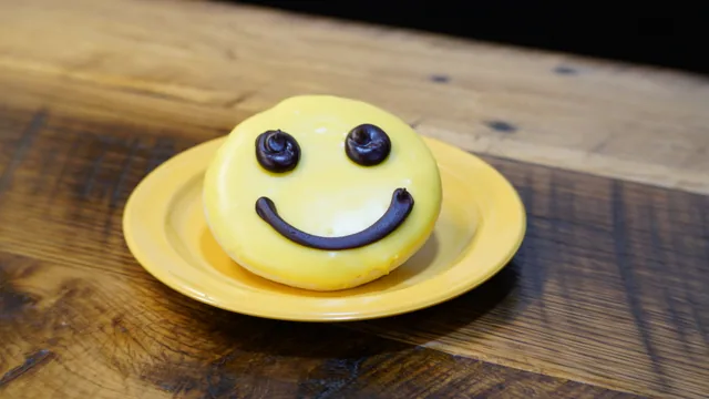 A round donut with yellow icing and a dark smiley face.