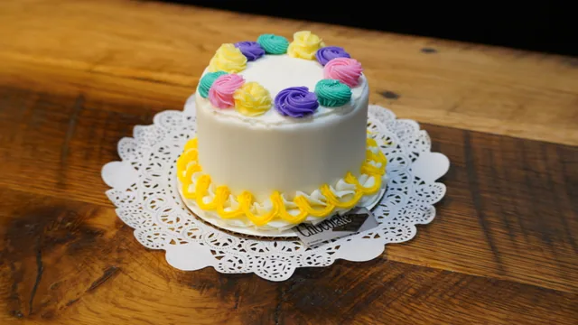 A small white cake topped with colorful icing swirls and a yellow base border.