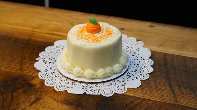 A small white cake topped with a piped orange carrot decoration.