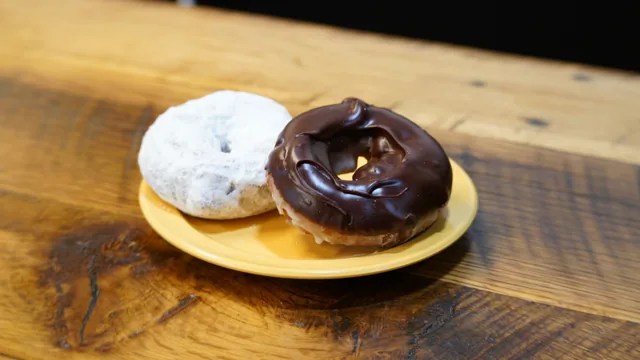 A powdered donut beside a chocolate-topped ring donut on a yellow plate.