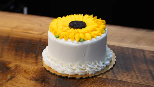 A white round cake topped with a large yellow sunflower decoration.