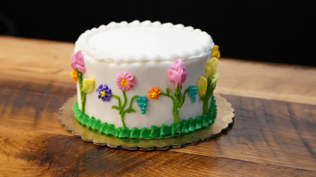 A white cake decorated with pink and purple flowers and green icing stems.