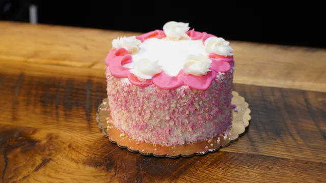 A small white cake with a pink top border, white icing swirls and pink crumbs on the sides.